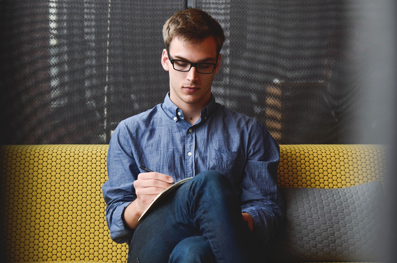 Hombre con lentes, sentado escribiendo en un cuaderno