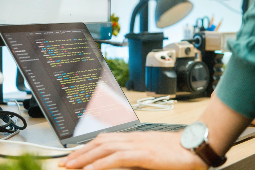 Mano de un hombre recargado en un escritorio mirando hacia una laptop con codigos de programacion abiertos