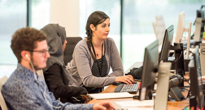 Tres personas sentadas trabajando en sus computadoras, dentro de una oficina
