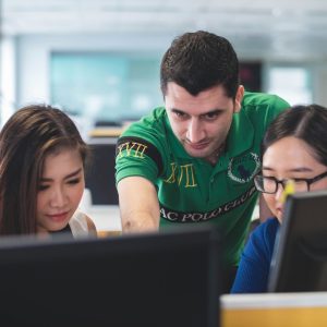 Dos mujeres sentadas prestando atencion, mientras un hombre señala a una computadora